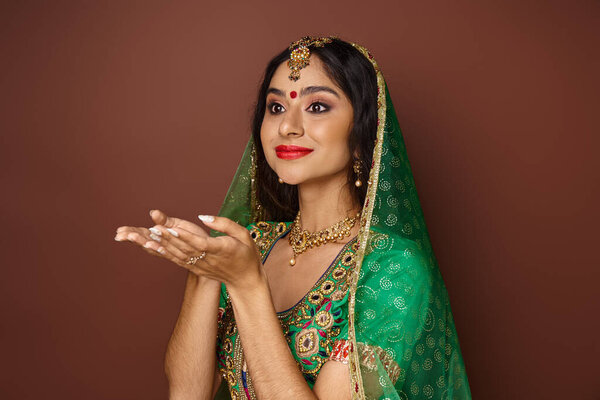 beautiful young indian woman in traditional clothes posing with open palms and looking away