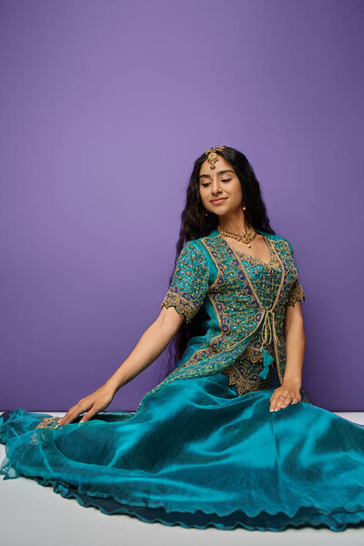 vertical shot of attractive indian woman sitting on floor in blue traditional sari and looking away