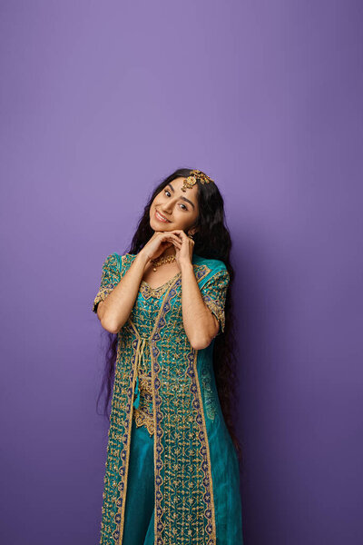 attractive young indian woman in national costume posing on purple backdrop and smiling at camera