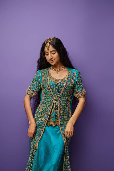 vertical shot of attractive indian woman in national clothing with accessories on purple backdrop