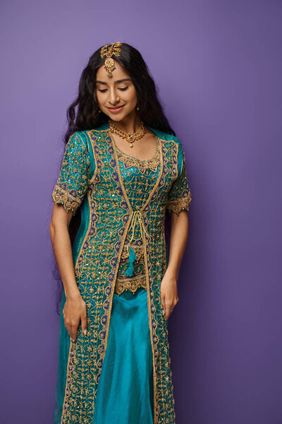 vertical shot of jolly young indian woman in blue sari with accessories posing on purple background
