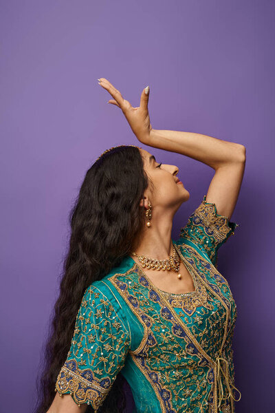 vertical shot of beautiful indian woman in blue sari gesturing while dancing on purple backdrop