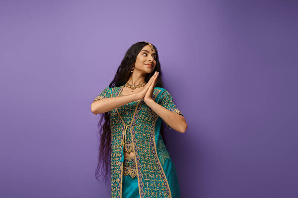pretty joyful indian woman in blue sari with accessories posing in motion on purple backdrop