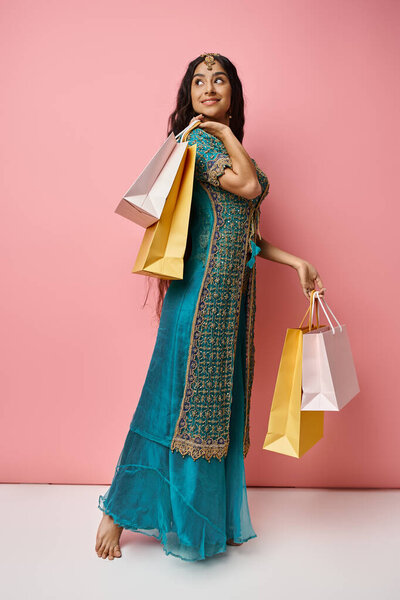 красивая индийская женщина позирует в профиль с пакетами покупок поворачивая голову и радостно улыбаясь