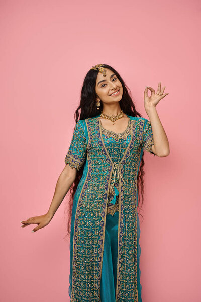 vertical shot of young indian woman in national costume gesturing and posing on pink background