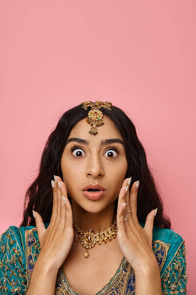 удивлена молодая индийская женщина в национальном костюме позирует с руками у лица с открытым ртом