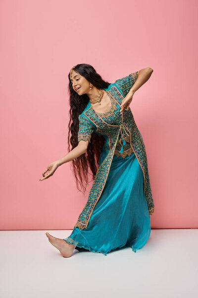 красивая индийская женщина в традиционном синем сари жестикулирует, танцуя на розовом фоне