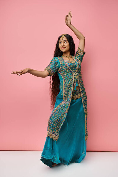 привлекательная молодая индийская женщина в национальной одежде жестикулирует, танцуя на розовом фоне