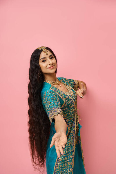 привлекательная молодая модель в синем традиционном сари, смотрящая на камеру на розовом фоне