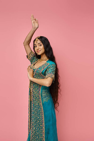 beautiful indian woman in blue sari with accessories gesturing on pink backdrop looking at camera