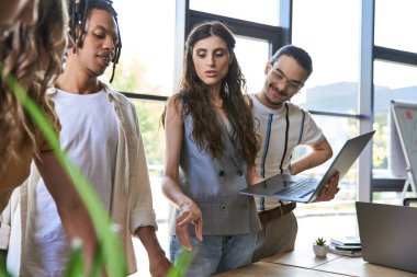 Kadın takım, ofiste çoklu etnik gruplarla yapılan toplantıda dizüstü bilgisayarla işaret ederek önde gidiyor.