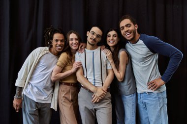 group photo of cheerful interracial colleagues looking at camera near black drape in office clipart