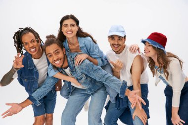 Neşeli Afro-Amerikalı erkek, çok ırklı arkadaşların yanında kadını sırtında taşıyor ve gri renkte eğleniyor.