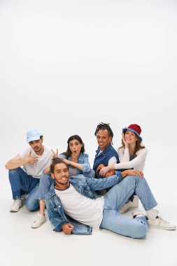 cheerful woman showing horns gesture near trendy african american man lying down on grey backdrop clipart