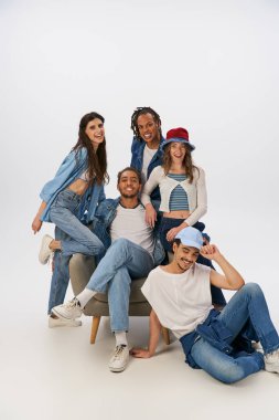 Mutlu Afrikalı Amerikalı adam gri üzerine poz veren çok ırklı arkadaşlarının yanında oturuyor.