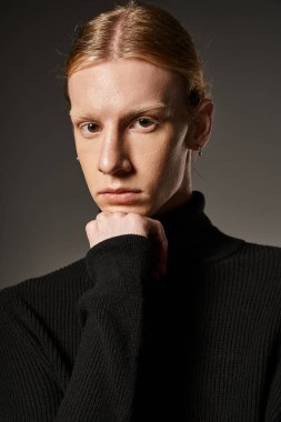 attractive non binary model in black turtleneck looking at camera with fist under chin, fashion clipart