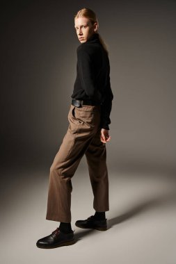 Siyah balıkçı yaka yakalı, kolları arkada poz veren, ikili olmayan genç ve çekici biri.