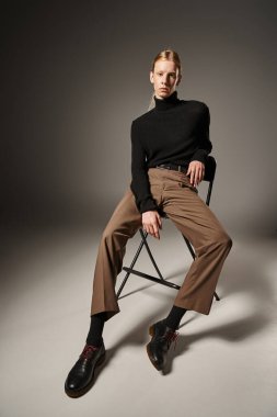 young red haired model in stylish black turtleneck sitting on black chair and looking at camera clipart