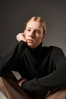 vertical shot of young non binary model sitting on floor with crossed legs and looking at camera clipart