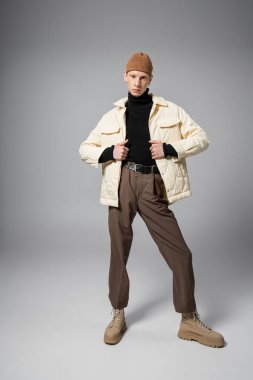 Sıcak kışlık ceketli ve bereli genç, ikili olmayan birinin kameraya bakarken dikey görüntüsü.