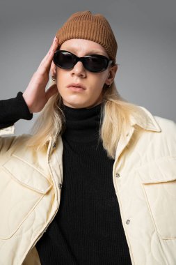 vertical shot of young non binary model in sunglasses and winter trendy jacket looking at camera clipart