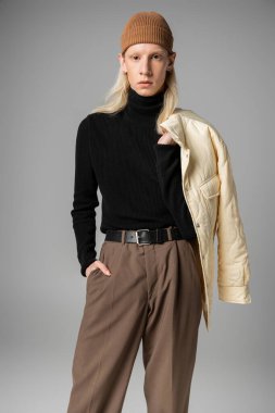 Kışlık ceketli ve cebinde tek elle poz veren genç, modaya uygun olmayan model.