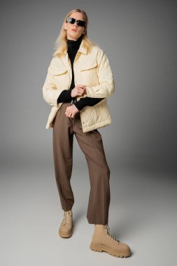 Gri arka planda duran güneş gözlüklü, kışın şık giyinen ikili olmayan çekici kişi.