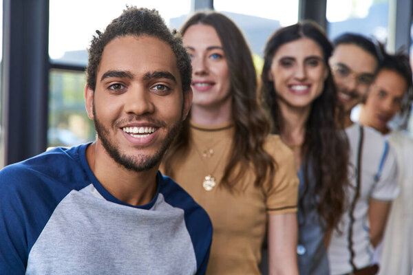 headshot of cheerful african american man smiling at camera near creative team in office, leadership