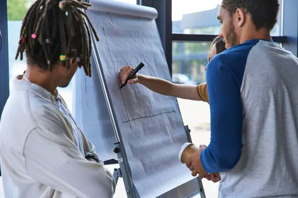 stock image creative woman drawing graphs on flip chart near african american colleagues in modern office