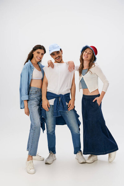 полная длина модного мужчины и привлекательных женщин в стильной одежде, стоящих на сером фоне