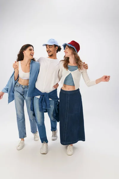 stock image full length of cheerful man and women in fashionable street wear walking together on grey backdrop