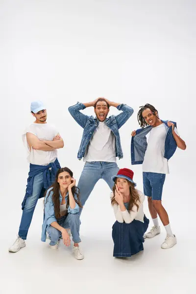 stock image excited multicultural men posing near stylish women squatting on grey backdrop, street style