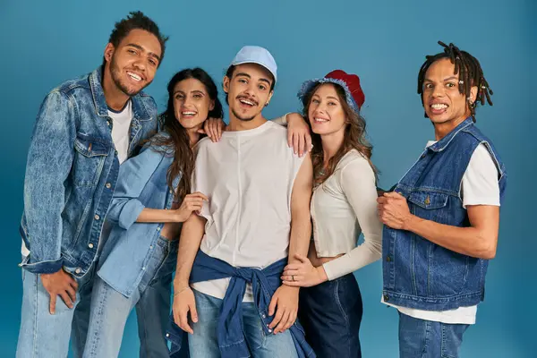 diverse group of excited interracial friends in trendy and denim clothes looking at camera on blue