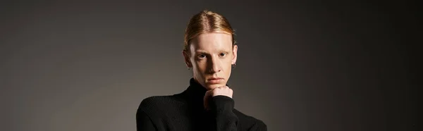 young non binary model in black turtleneck looking at camera with hand under chin, fashion, banner