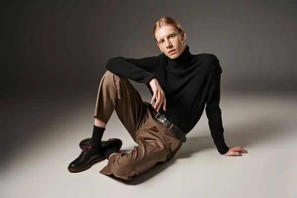 young non binary person in black turtleneck sitting on floor and looking at camera, fashion concept