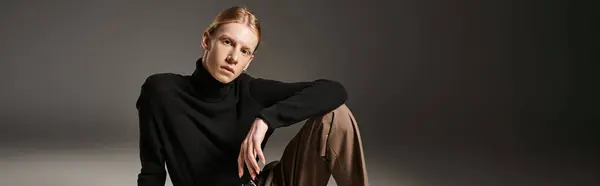 attractive non binary person in black turtleneck sitting on floor and looking at camera, banner
