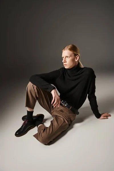 good looking non binary person in black turtleneck and brown pants sitting on floor, fashion