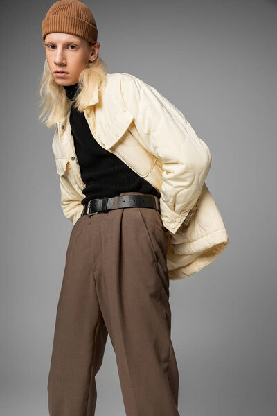 vertical shot of young attractive non binary person in beanie hat looking at camera on gray backdrop