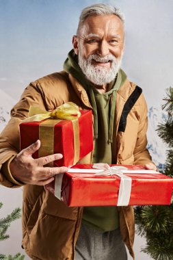 Noel Baba gibi giyinmiş neşeli bir adam elinde kırmızı hediyeler ve kameraya içten bir gülümseme, kış konsepti.