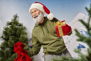 Noel Baba gibi giyinmiş neşeli bir adam hediye paketi ve hediye paketi ile dağ arkası, kış