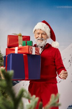 Noel Baba kostümlü neşeli adam elinde hediyelerle elini bir kenara koyuyor, kış konsepti.