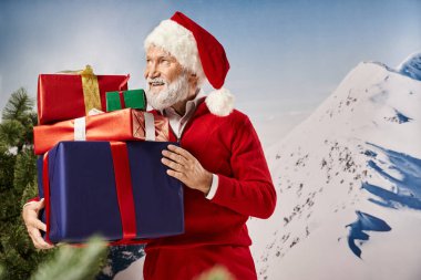 Noel Baba kostümü giymiş yakışıklı bir adam. Elinde hediyeler, gülümsüyor ve uzaklara bakıyor. Kış konsepti.