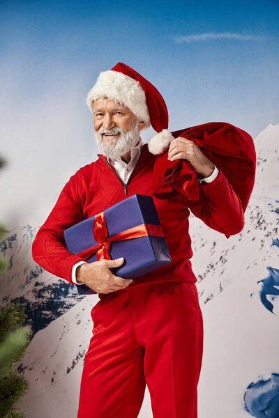 весёлый мужчина в костюме Санты, искренне улыбается и держит подарок и подарочную сумку, зимняя концепция