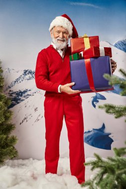 Kırmızı Noel Baba kostümlü neşeli bir adam. Elinde karlı bir zemin ve kış konsepti olan hediyeler var.
