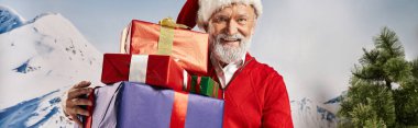 Beyaz sakallı, Noel Baba kostümlü neşeli adam kameraya, kış konseptine, afişe hediyeler gösteriyor.