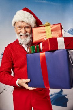 Elinde hediyeler, karlı dağ zeminiyle şık yakışıklı Noel Baba, kış konsepti.