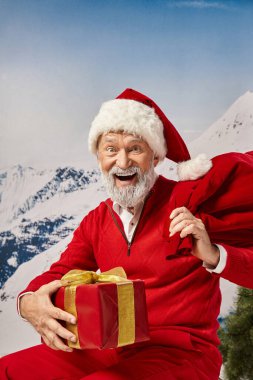 Noel şapkalı neşeli Noel Baba hediye çantasıyla kameraya gülümsüyor, kış konsepti.