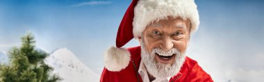 Şapkalı neşeli Noel Baba kameraya mutlu bir şekilde gülümsüyor. Dağ arkası, kış konsepti, bayrak.