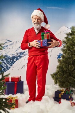 Kırmızı şapkalı neşeli Noel Baba hediyelerle poz veriyor ve kameraya gülümsüyor, kış konsepti.