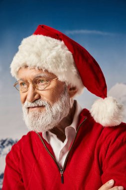Noel Baba gibi giyinmiş, karlı arka planda poz veren yakışıklı bir adam başka tarafa bakıyor, kış konsepti.